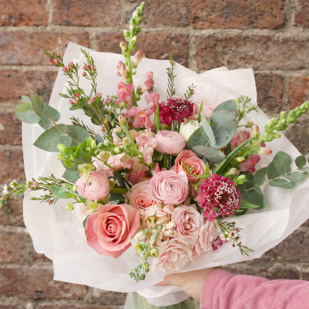 Bouquet of pink and red flowers with greenery against a brick wall.