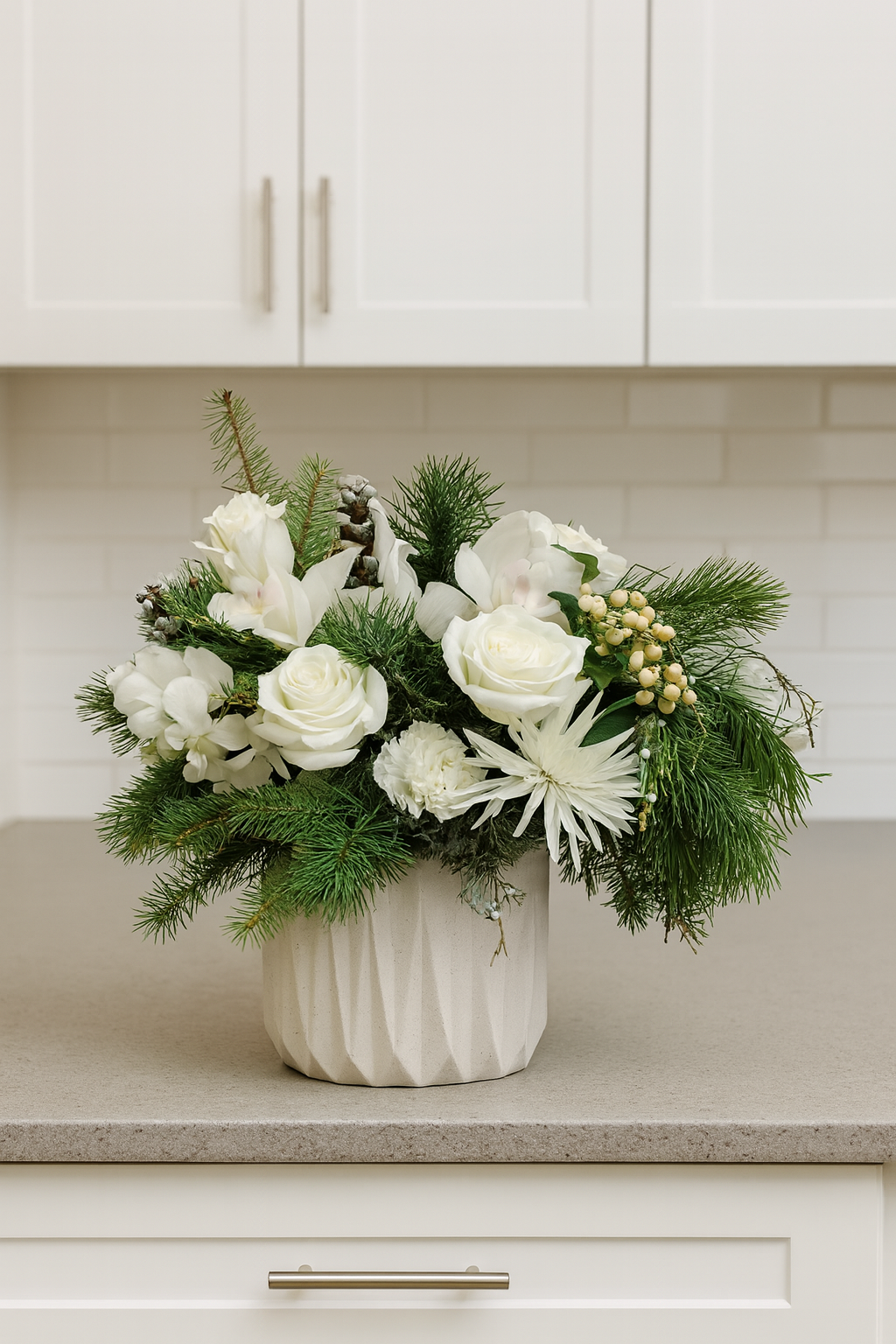 Floral arrangement with white flowers and greenery in a white vase on a kitchen counter.