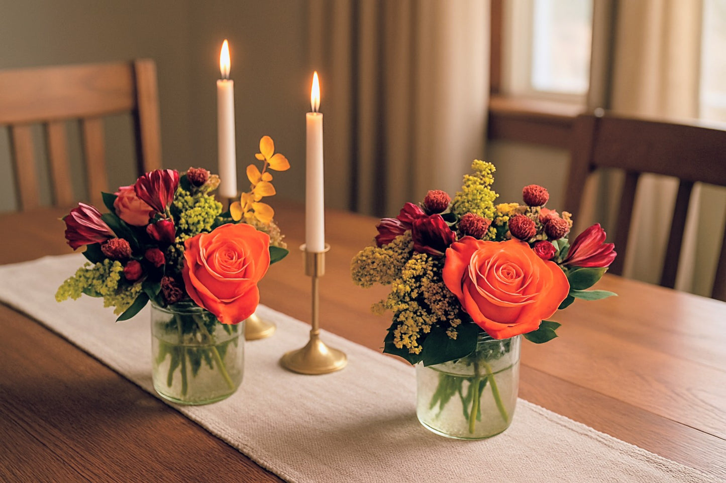 Two flower arrangements in glass vases on a wooden table with candles.