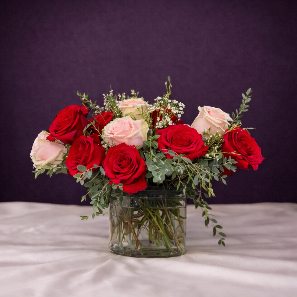 Bouquet of red and pink roses in a clear vase on a white surface with a purple background
