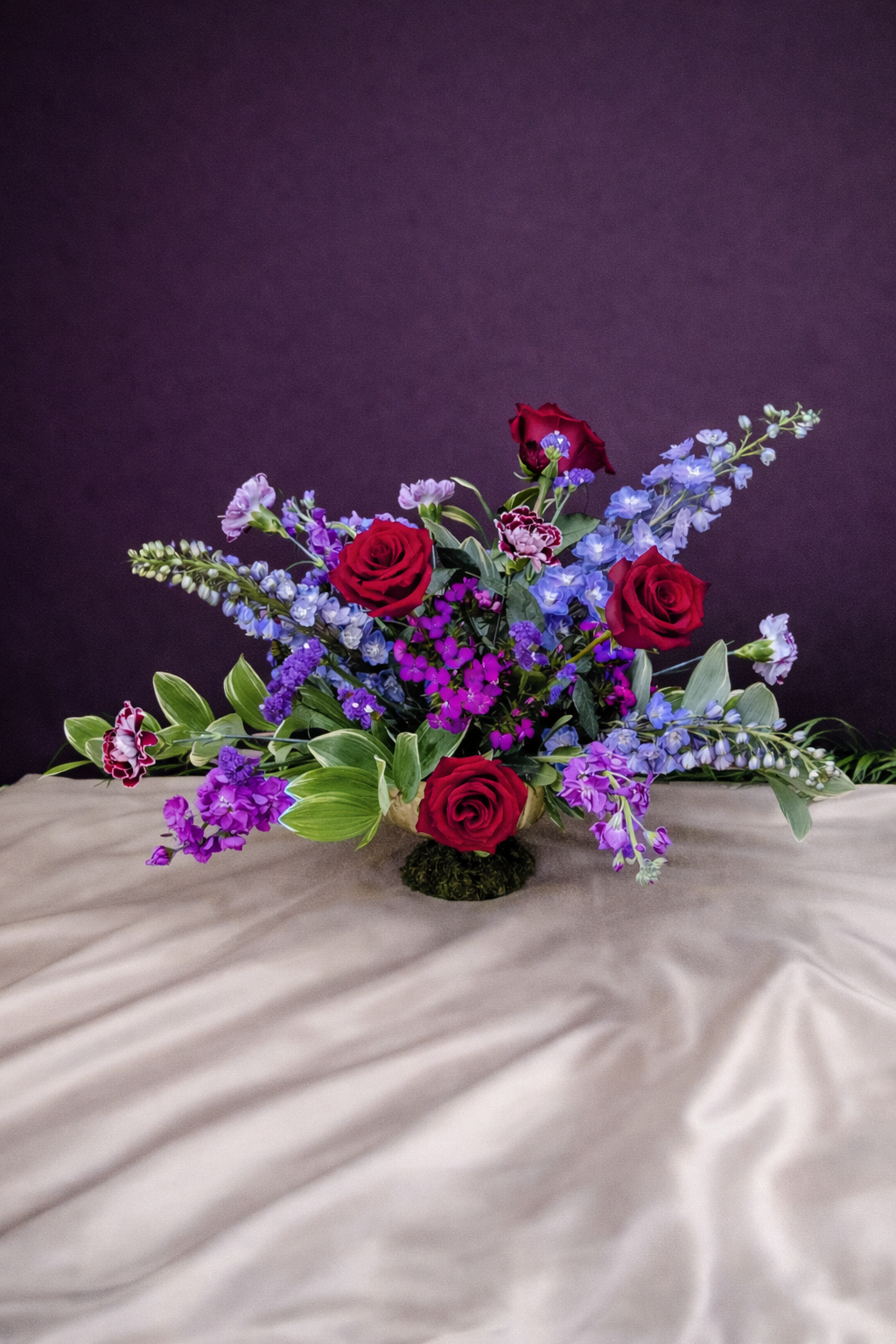 Floral arrangement with red roses and purple flowers on a textured surface with a dark background