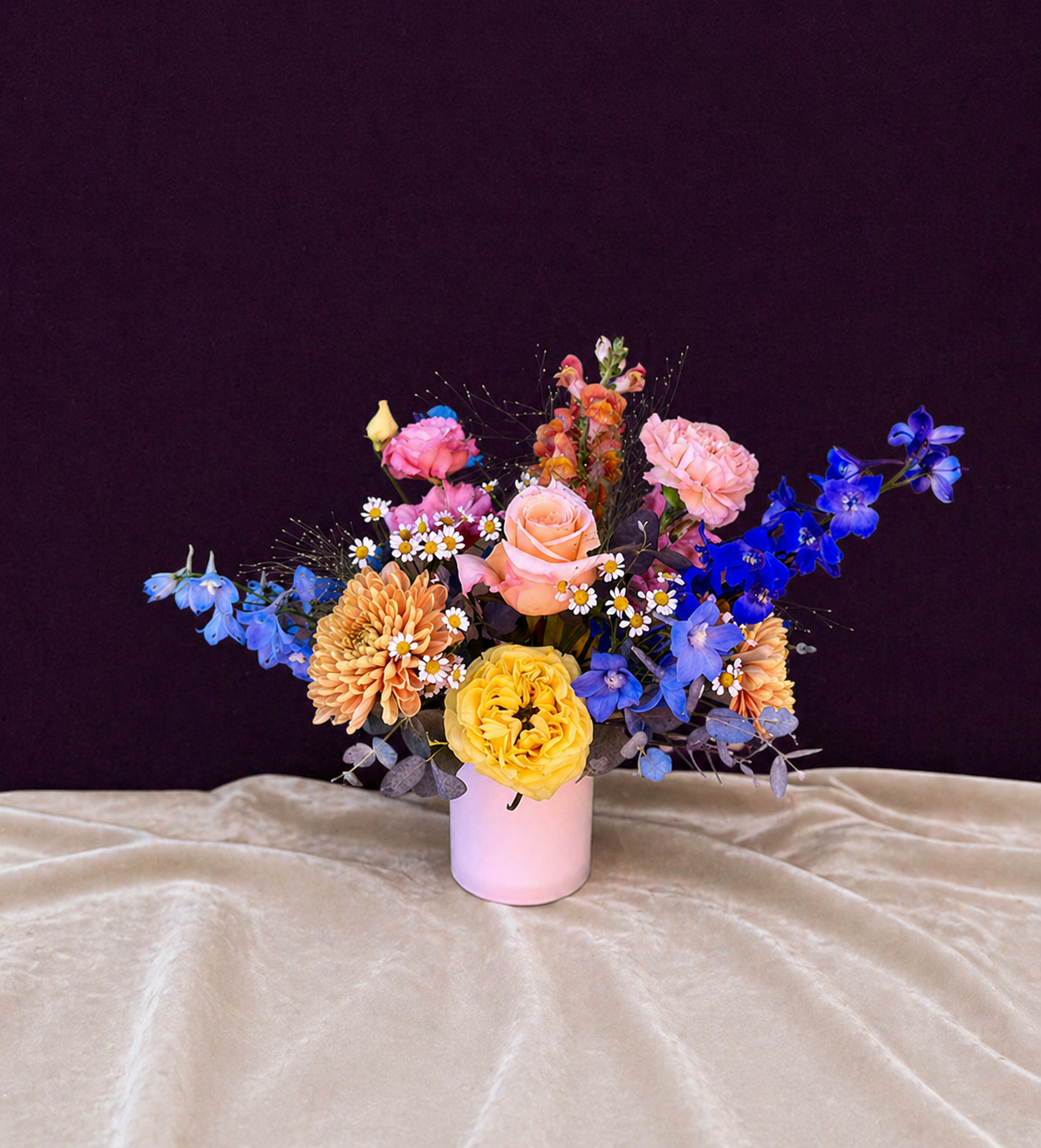 Colorful flower arrangement in a pink vase on a beige surface with a dark background