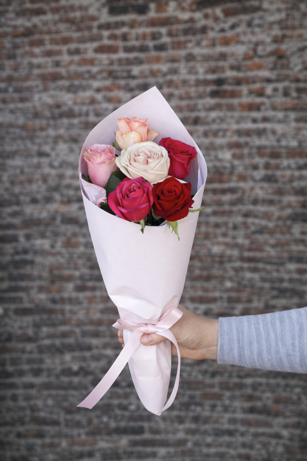 6 roses in a bouquet in front of a brick wall