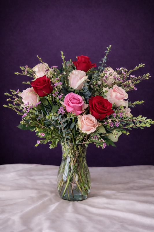 Bouquet of red, pink, and white roses in a clear vase on a purple background