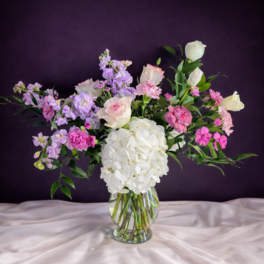 Bouquet of flowers in a clear vase on a white surface with a dark purple background