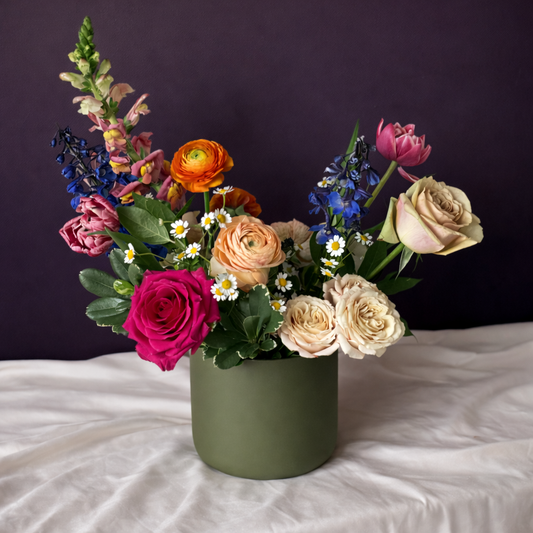 Colorful flower arrangement in a green vase on a white surface with a dark background