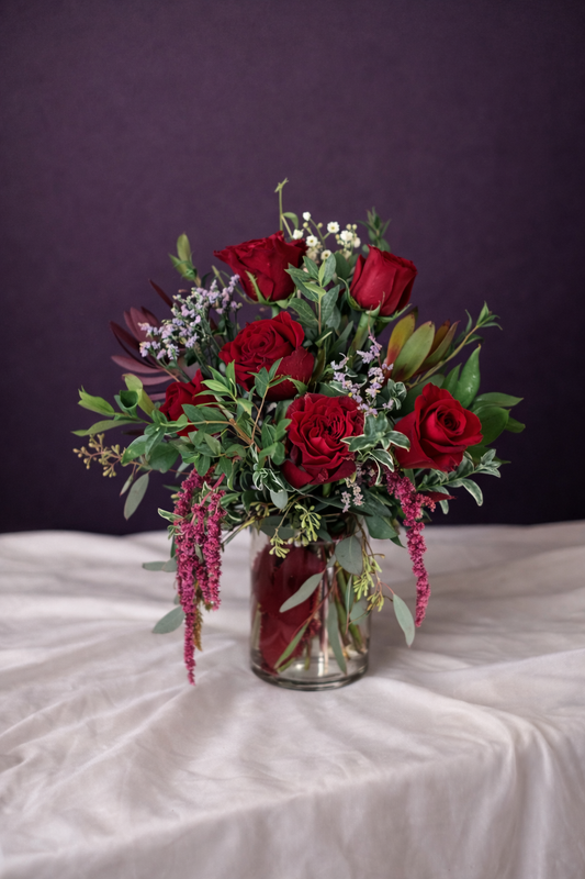 Bouquet of red roses and greenery in a clear vase on a white surface with a dark background
