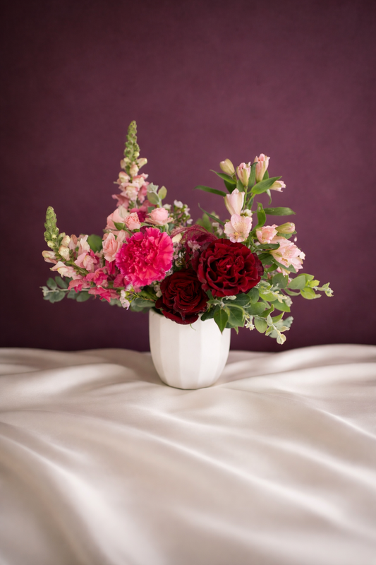 Floral arrangement in a white vase on a satin surface with a purple background