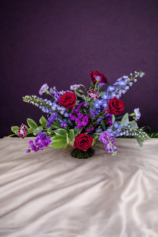 Floral arrangement with red roses and purple flowers on a textured surface with a dark background